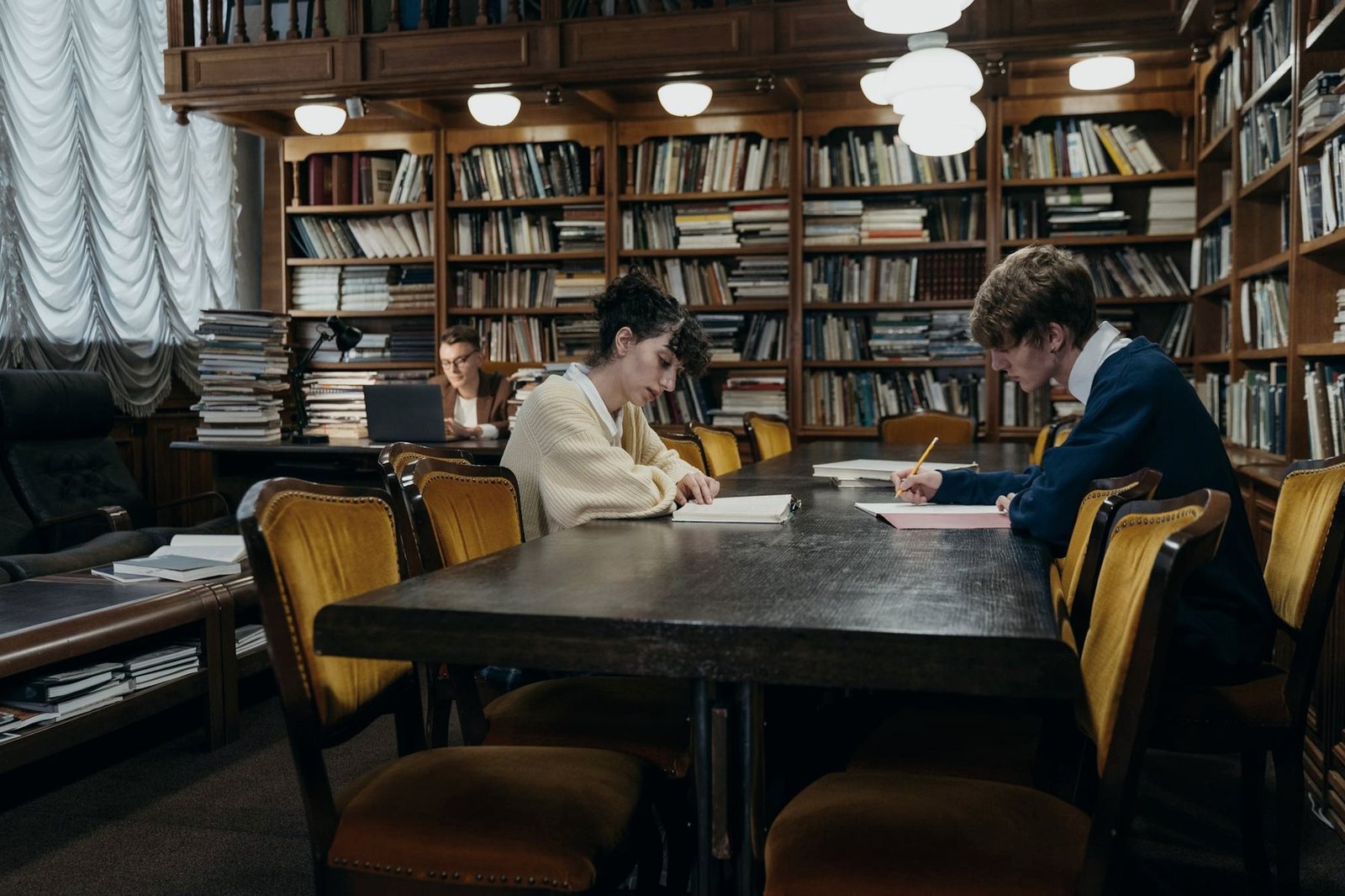 Two students studying at a long table in a traditional wood-paneled library